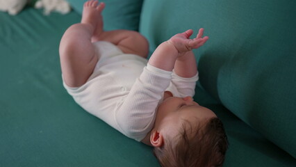 Baby lying on the couch, holding hands together while staring upward, dressed in a cozy onesie. a peaceful and relaxed moment of the baby at rest