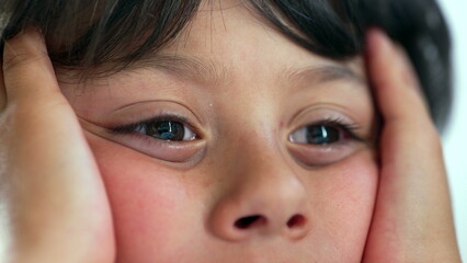 Child pressing face into hands with a distant gaze, lips slightly parted, portraying a sense of wonder and thoughtfulness while sitting quietly, highlighting raw childhood emotion