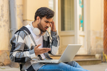 Displeased Indian man using laptop typing browsing working, loses becoming surprised sudden lottery...