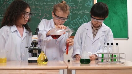 Caucasian student doing experiment and pouring biochemical solution surrounded by curious children waiting for discover new innovation at laboratory. Diverse happy student doing experiment. Pedagogy.