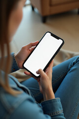 woman sits indoors wearing jeans looking smartphone white screen background