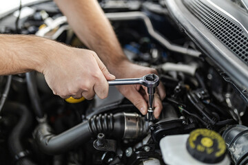 A mechanic repairs an engine using a ratchet wrench in a car at a workshop during the daytime