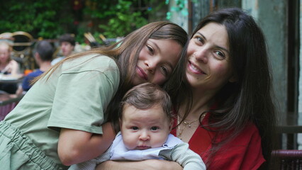 Mother and her two children sharing a warm embrace outdoors. Young girl hugs her mother and baby sibling, expressing love and closeness in a relaxed and joyful family moment