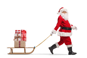 Santa Claus alking and pulling a wooden sled with presents