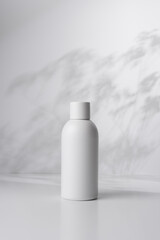 White bottle on a light background with shadows of leaves