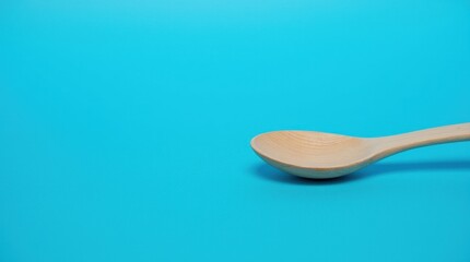 A wooden spoon rests on a bold electric blue backdrop, with its natural texture standing out against the vibrant background, creating a striking visual contrast.