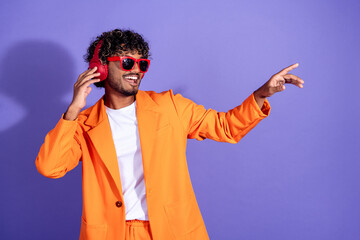 Fototapeta premium Photo of cheerful positive guy dressed orange jacket enjoy songs headphones emtpy space isolated purple color background