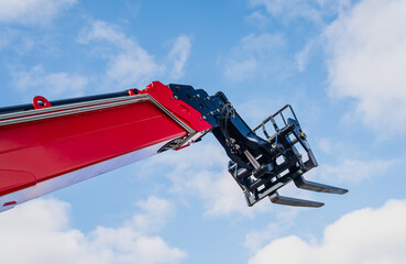 Big red industrial boom lift hydraulic system of very modern construction equipment and metal fork carriage next to blue sky background © K