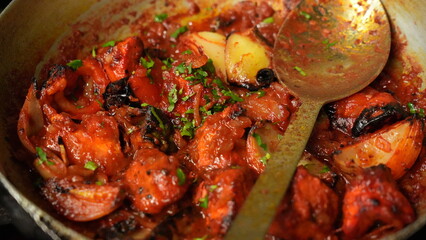 Dish of cooked chicken, glistening in a rich, reddish-brown sauce, the sauce features chunks of...
