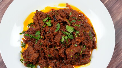 Spicy meat dish garnished with fresh green herbs, served on a white plate. the meat appears tender...