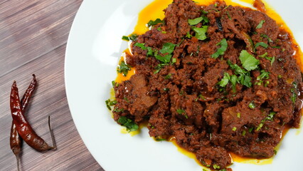 Spicy meat dish garnished with fresh green herbs, served on a white plate. the meat appears tender and flavorful, contrasting with a bright, oily sauce. accompanying the plate are dried red chilies.
