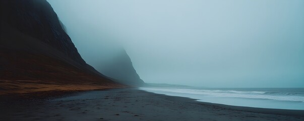 Dramatic black sand beach with foggy mountain cliffs in Nordic twilight. Minimalist seascape of Icelandic volcanic coastline. Moody nature photography