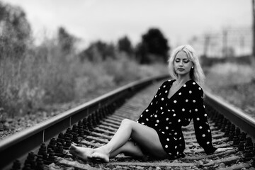 Portrait of a young beautiful blonde girl on the railway tracks. Black and white photo.