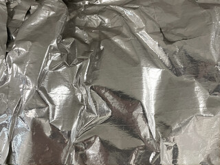 Silver metal crumpled kitchen foil sheet closeup, wrinkled grunge texture as background. Shiny,...