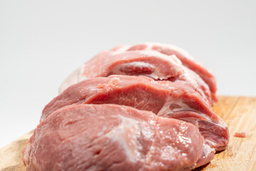 A slab of meat is cut into slices and placed on a wooden cutting board. Concept of preparation for cooking or serving the meat Pork meat isolated on a white background.