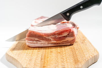 A knife is cutting a piece of meat on a wooden cutting board Pork meat isolated on a white...