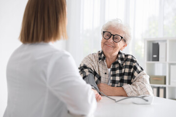 Doctor measuring patient's blood pressure at table in hospital