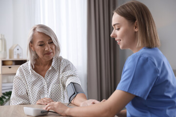 Healthcare worker measuring patient's blood pressure at wooden table indoors