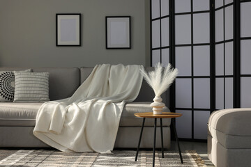 Comfortable sofa with plaid and folding screen in living room. Interior design