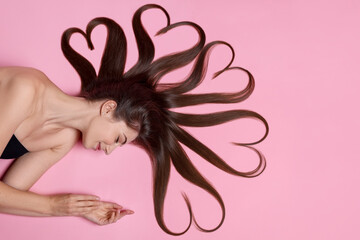 Beautiful young woman with hair in shape of hearts on pink background, top view