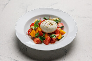 Vegetable salad with burrata cheese on a large white plate. Menu.