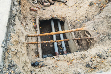 Excavation site with exposed utility pipes and rusty rebar in a residential area during midday