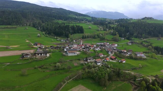 Aerial footage of a mountain valley with patches of clouds drifting over green fields and small villages, surrounded by forested hills.