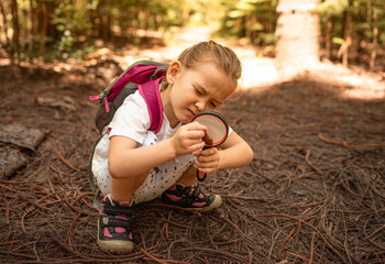 Little child exploring nature forest with magnifying glass
