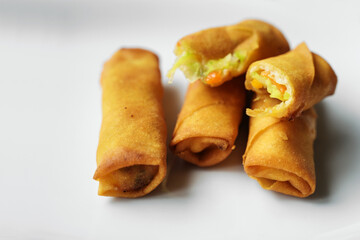 Small crispy fried spring rolls filled with vegetables on a white plate, appetizer in a Chinese restaurant, high angle view from above, cop space, selected focus