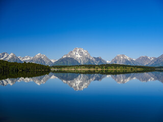 A perfect summer day reflections of snow-covered Grand Teton mountains in a mountain lake  in Wyoming
