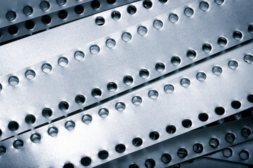 A series of metal strips with holes in them. The holes are evenly spaced and the strips are of varying thickness. Concept of order and precision, as well as a sense of industrial or mechanical nature