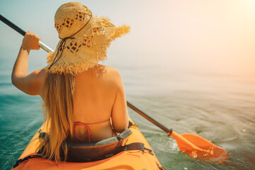 Woman in kayak back view. Happy woman with long hair in a swimsuit and hat floating in kayak on the sea. Summer holiday vacation. Summer holidays vacation at sea.