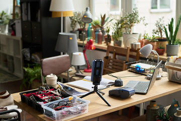 Workplace of owner of modern thrift shop with smartphone on tripod, laptop, payment terminal, open copybook and accessories