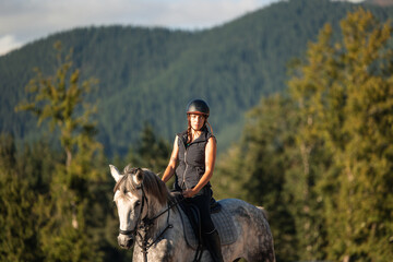 Female rider guiding her horse through the mountains while looking at the camera