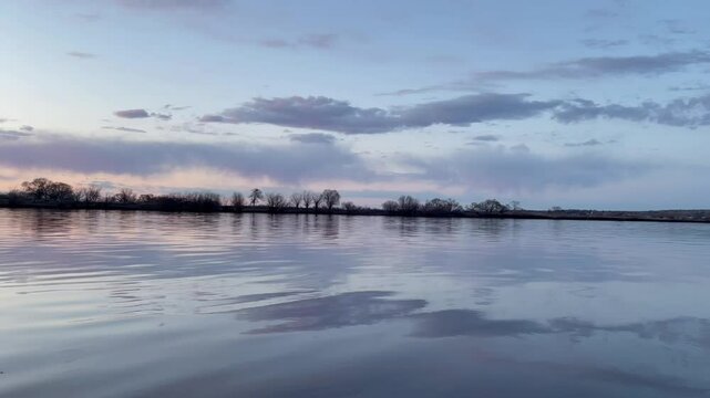 Colorful sunset sky with dark clouds with trees reflection on calm river water 