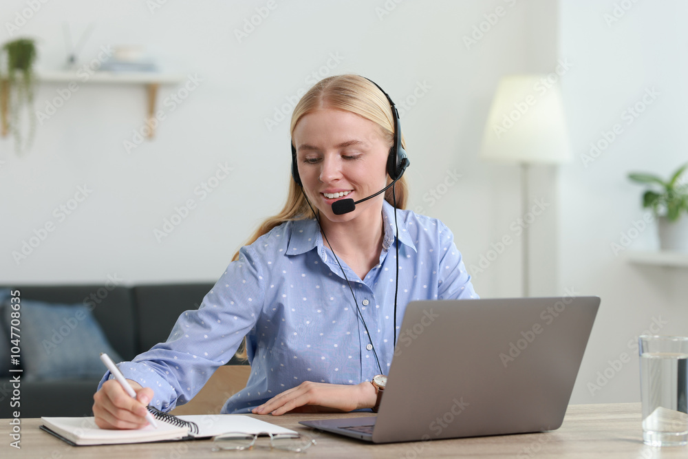 Poster interpreter in headset taking notes while working with laptop at table indoors