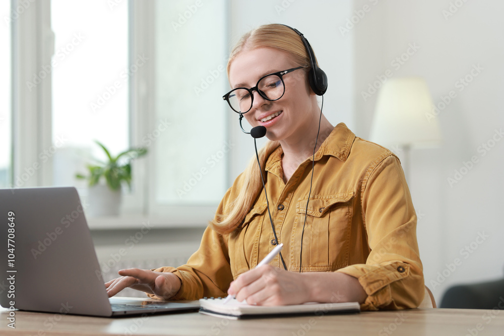 Poster interpreter in headset taking notes while working with laptop at table indoors