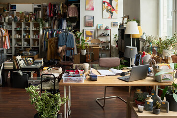 Interior of spacious modern thrift shop with workplace of clerk surrounded by variety of goods such as secondhand attire and footwear