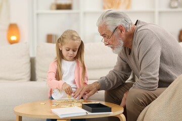 Grandpa and his granddaughter playing dominoes at table indoors