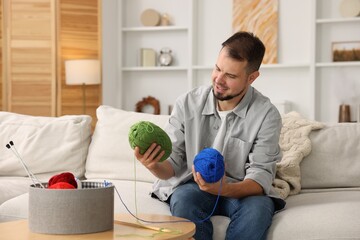 Fototapeta premium Man with colorful yarns on sofa at home. Knitting material