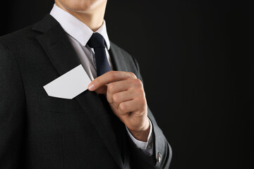 Man taking blank business card from pocket of his jacket on black background, closeup. Mockup for...