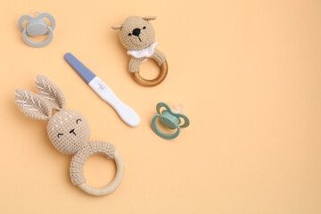 Pregnancy test, baby rattles and pacifiers on pale orange background, flat lay. Space for text