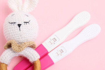 Pregnancy tests and baby rattle on pink background, closeup