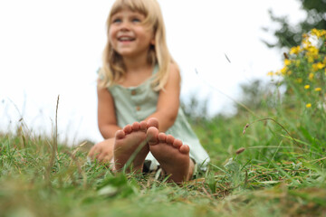 Fototapeta premium Barefoot little girl on green grass at meadow, selective focus. Child enjoying beautiful nature