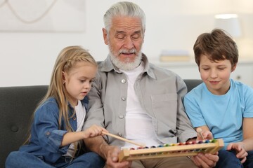 Grandpa and his grandkids playing toy xylophone on sofa at home