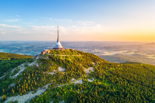 This aerial view captures Jested mountain in Liberec, Czechia, showcasing the iconic hotel and TV transmitter amid sprawling greenery at sunset, revealing stunning landscapes.
