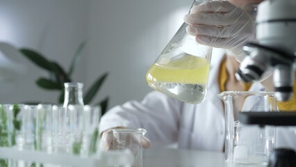 A scientist wearing white protective gloves is shaking up a yellow chemical solution inside an...
