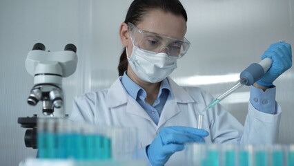 Scientist woman researcher, wearing a lab coat, mask, blue gloves and safety glasses, is using a...