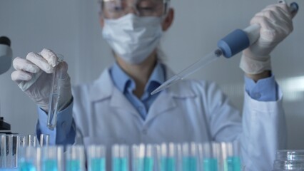 Scientist woman, wearing a lab coat, mask, blue gloves and safety glasses, is using a micropipette to drop a liquid into a test tubes. Medicine and science