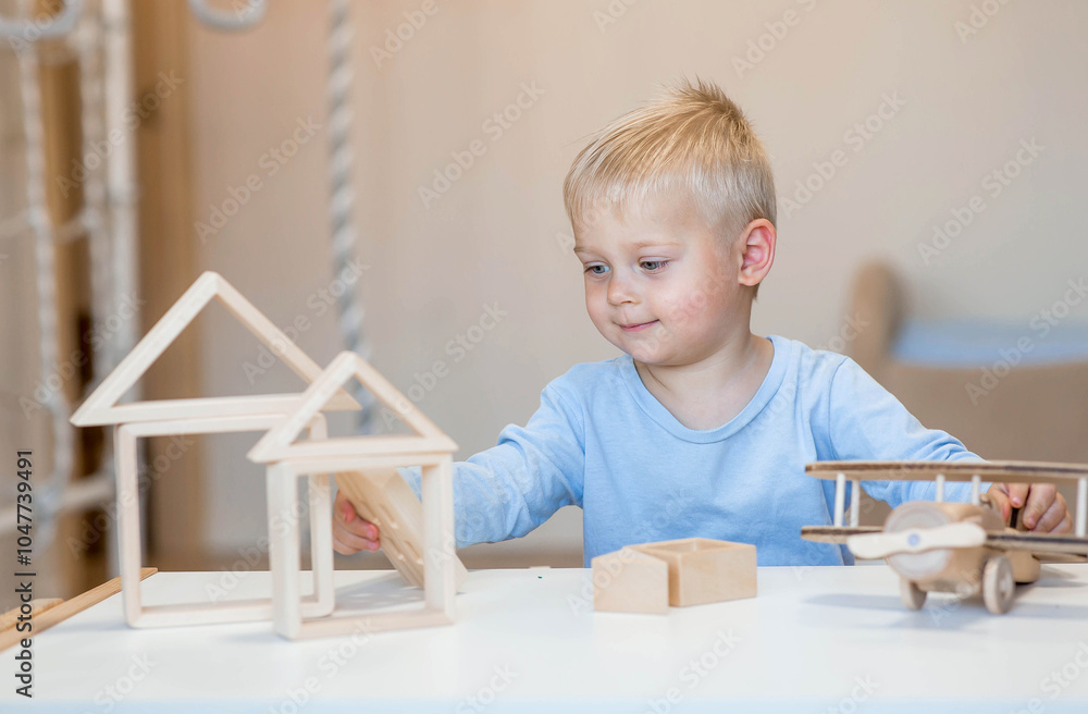 Wall mural a little boy of 2 years old is playing a developing logistics constructor. children's wooden toys. m